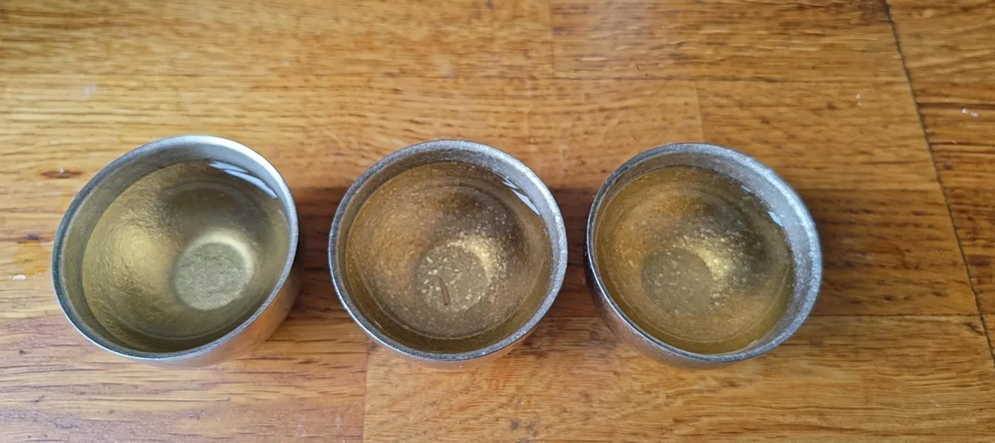 三只锡杯并排摆在一张旧木桌上,三杯茶汤都是相近的金黄色,几乎看不出深浅差别