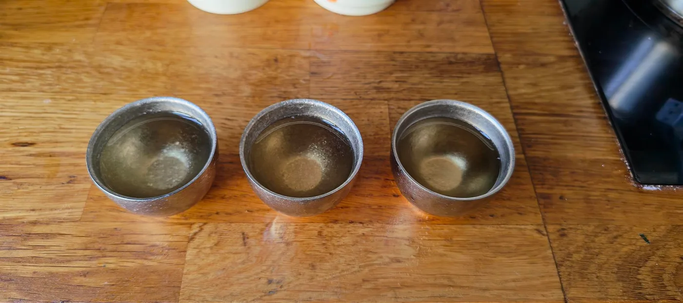 三只锡杯并排摆在一张旧木桌上,三杯茶汤都是相近的浅金色,深浅差别很小